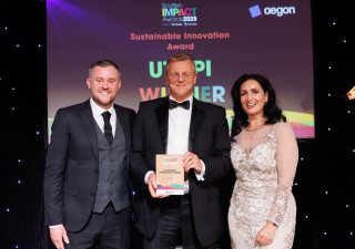 Two gentlemen in black tie stand with a woman in a formal dress holding an award.